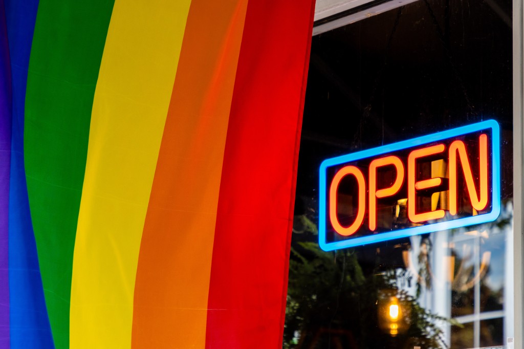 Neon OPEN sign in a store window beside a rainbow pride flag